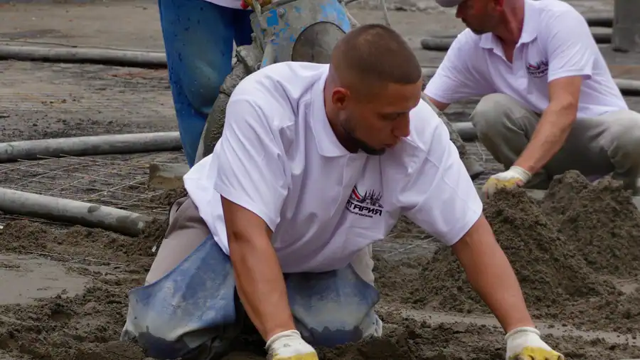 Construction workers expertly level wet concrete for a smooth finish on a building site.