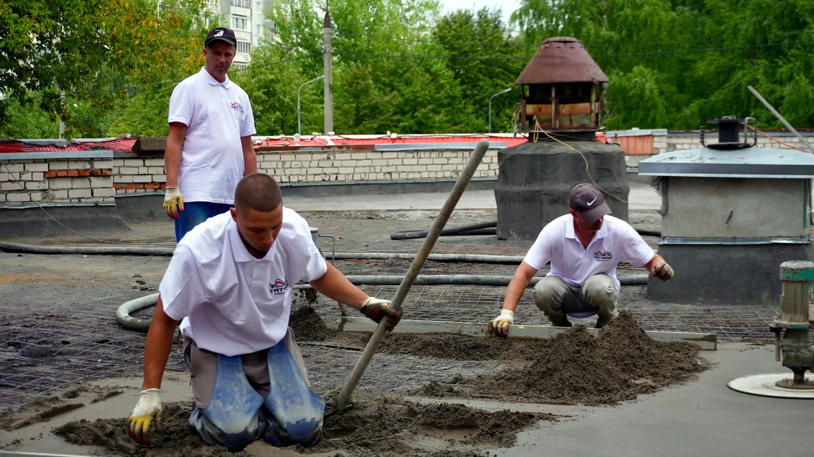 Three workers troweling and leveling cement on a rooftop construction project.