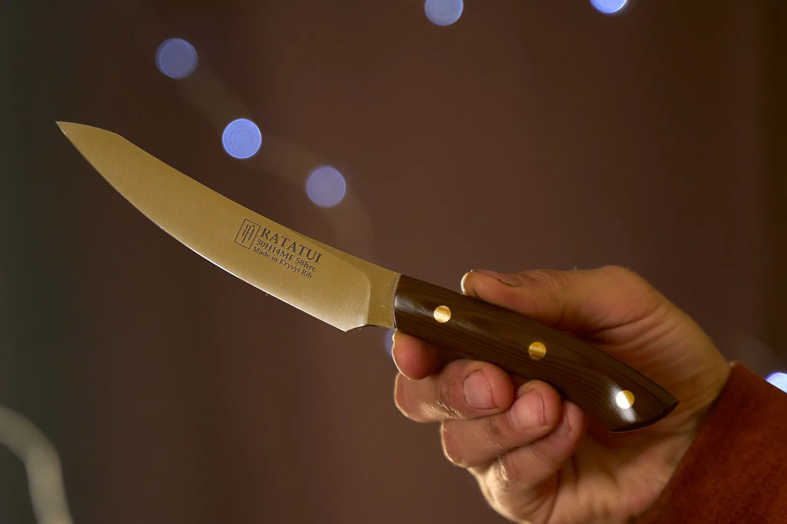 Close-up of a handcrafted kitchen knife with a wooden handle held by a hand, perfect for culinary use.