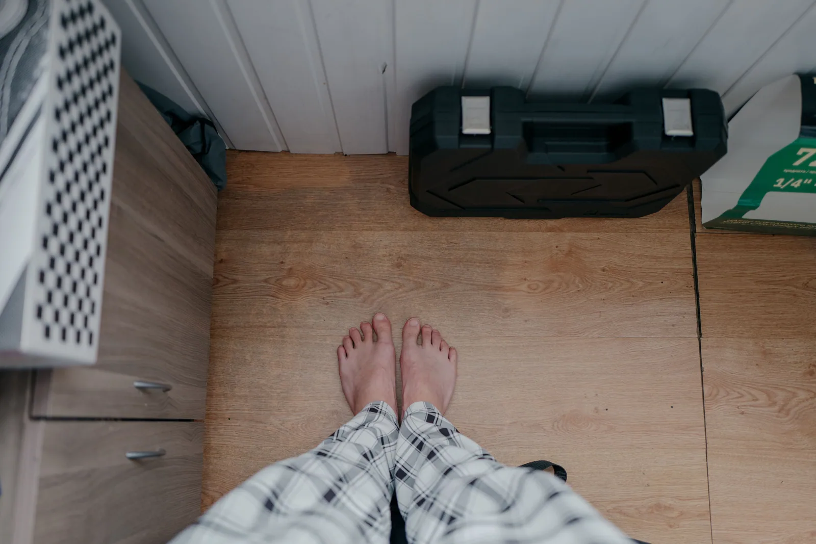 Overhead view of bare feet in pajamas on wooden floor indoors with tool box nearby.